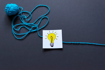Light bulb drawn on note and a ball of thread on the dark background.