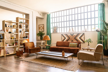 Interior design / decoration. Spacious living room in bright industrial loft with indoor green plants. Relax zone with brown sofas and armchairs.