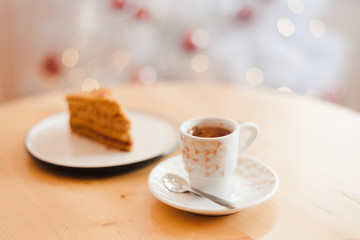 Italian coffee Cup and honey cake on the table near the Christmas tree with white bokeh