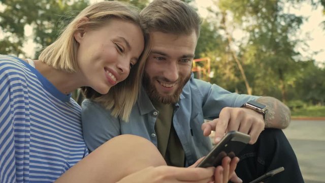 A young beautiful couple man and woman are watching something interesting on the smartphone on the sport area