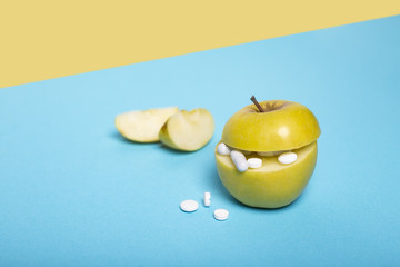 Medicine concept with fresh apple and tablets. Piece of apple. Genetically modified fruit on blue and yellow background