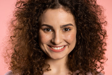 Young curly woman with trendy glitter freckles make-up. Portrait of beautiful girl on pink studio background