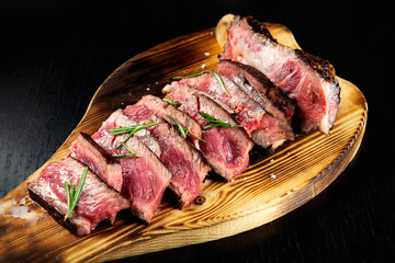 Juicy Beef Rib Eye Steak slices slightly salted, with herbs and spices on wooden board. Fresh grilled meat. Dark black background