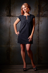 Naklejka premium Studio Portrait of Beautiful young woman with ginger hair in little black dress against dark background.