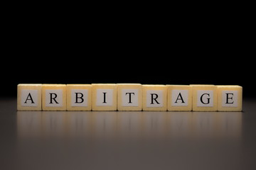 The word ARBITRAGE written on wooden cubes isolated on a black background...