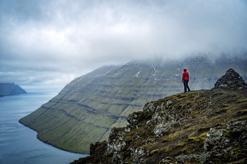 Female traveler standing at top of mountain and enjoying spectacular view over Faroe Islands fjords.