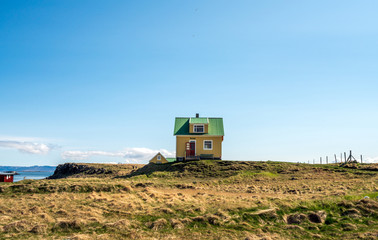 Fototapeta premium Yellow house on Flatey Island in Iceland just outside Stykkisholmur and the Westfjords. Blue sky and sunny weather. Explore and traveling concept.