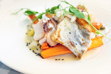 Delicious fillet of cod fish with carrots, leeks and mushrooms in white plate ready to be served