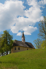 Fototapeta na wymiar chapel St Georg and trees at Weinberg hill, spring landscape Schliersee. blue sky with clouds