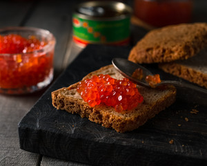 Salmon caviar on rye bread on dark wooden rustic background