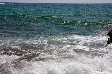 The frothy waves of the sea break on the rocks and on the beach.