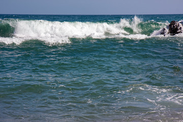 The frothy waves of the sea break on the rocks and on the beach.