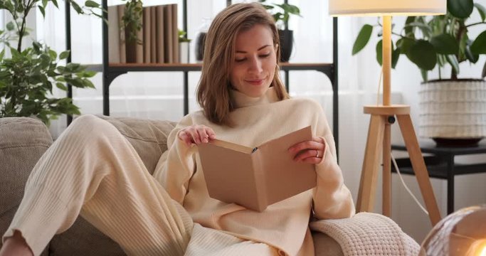 Happy woman reading a book while relaxing on sofa at home