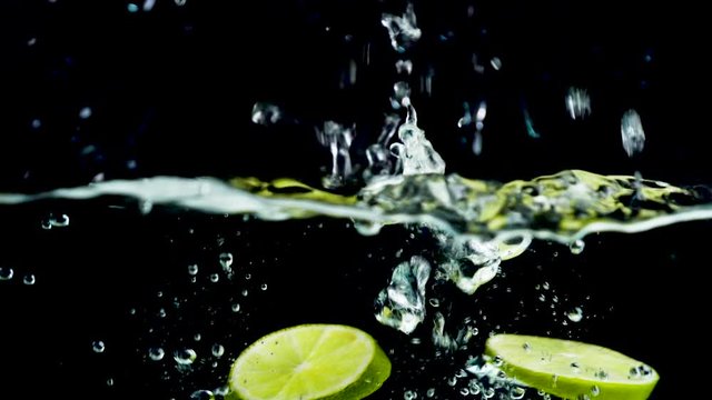 green lemon falling in water on black background- slowmotion