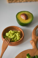 Bowl with guacamole and ripe avocado. Toast with avocado, arugula and pumpkin seeds on a wooden board in the shape of deer antlers.