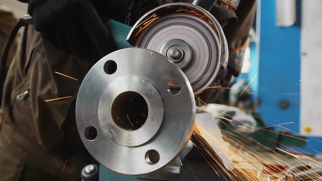 worker grinds flange of pumping system with sparks closeup