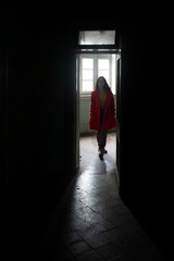 Young woman dressed in red walking through the open door of an abandoned room