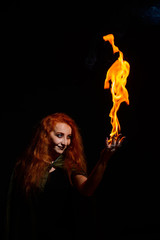 An ominous witch with long curly hair holds a magical fire. Tongues of flame on the palms of a...