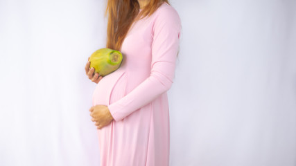A close up photo of a pregnant young woman holding a papaya next to her belly showing the size of the baby in a beautiful dress. Photos of fetal growth at 22 weeks pregnancy.