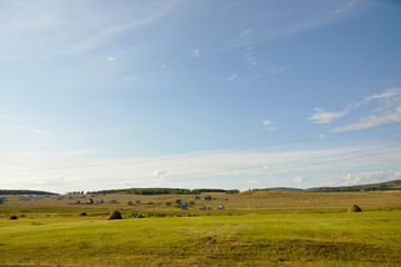 Fototapeta premium Light white clouds in the warm summer sky over village with small houses far away in the fields. Travelling. People living 