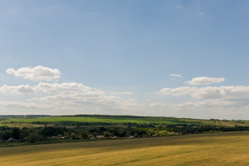 Light white clouds in the warm summer sky over village with small houses far away in the fields. Travelling. People living