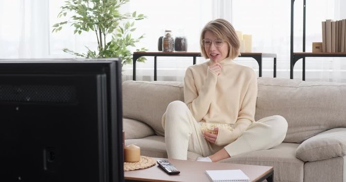 Woman laughing while watching tv and eating popcorn at home