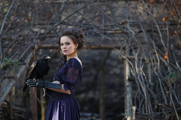 A girl walks through the winter forest with a raven in her hand.