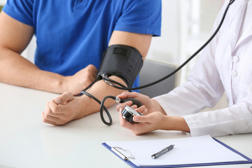Doctor measuring blood pressure of young man in clinic