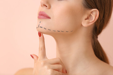 Young woman with marks on her face against color background, closeup. Concept of plastic surgery