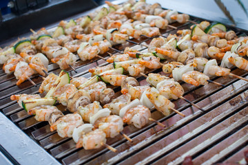 Outdoor picnic scene of seafood bbq with delicious shrimp on skews and prawn spits on a grill 