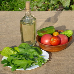 Vegetable oil in a bottle, fresh vegetables and greens on the table in the garden