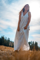 Fototapeta na wymiar Rural lifestyle, a young caucasian blonde with a long white dress and a white hat in the dry wheat field