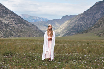 A girl walks through the meadow against the backdrop of the mountains. Prayer.