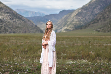A girl walks through the meadow against the backdrop of the mountains. Prayer.