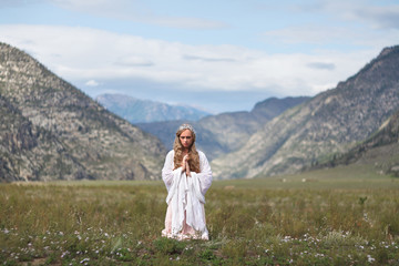 A girl walks through the meadow against the backdrop of the mountains. Prayer.