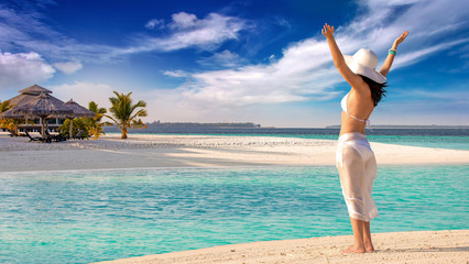 woman with raised arms wearing bikini and hat on the beach in Maldives