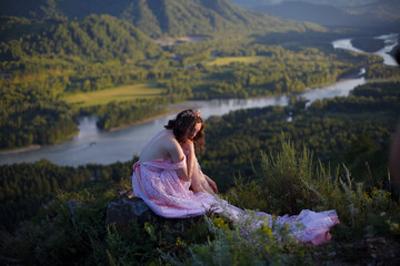 A girl in a pink dress with a long train. Bird's-eye. On the top of the mountain. Photosession in Altai