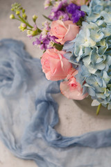 Top View Bouquet of Pink Roses, Blue Hydrangea, and Purple Flowers in a Clear Vase on Neutral Background with Blue Fabric in background