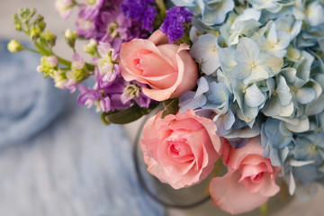 Top View Bouquet of Pink Roses, Blue Hydrangea, and Purple Flowers in a Clear Vase on Neutral Background with Blue Fabric in background
