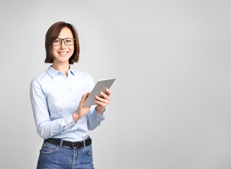 Beautiful woman with tablet in hand on grey background