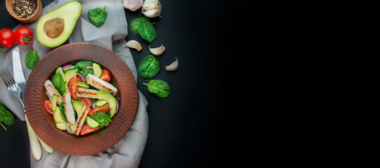 Fototapeta na wymiar A healthy salad of chicken breast, fresh vegetables, spinach leaves, avocado and tomatoes on a dark background. Salad of greens with meat. The concept of diet food. Copy space. Benner food.