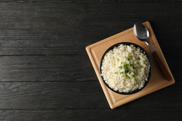 Board with bowl of delicious rice on wooden background, top view