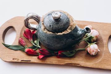 Teapot and cup of herbal tea on wooden background with fresh flowers on white table