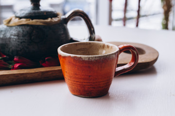 ceramic pot and orange cup on window background with flowers