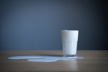 glass on wooden table with milk spilled over in a puddle