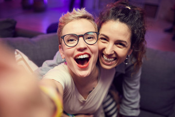 Portrait of two excited friends smiling at camera during selfie portrait