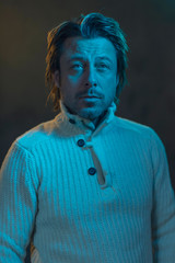Man wearing white woolen sweater illuminated by yellow and blue light.