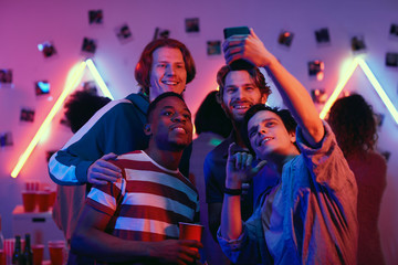 Fototapeta na wymiar Group of young boys making selfie portrait on mobile phone while having fun at a party