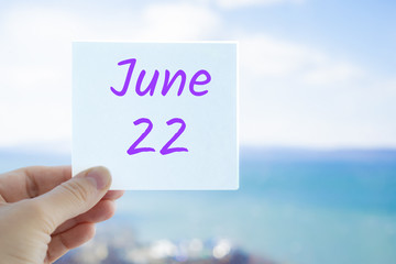 June 22nd. Hand holding sticker with text June 22 on the blurred background of the sea and sky. Copy space for text. Month in calendar concept