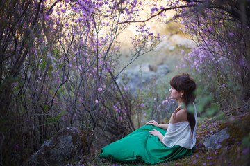A girl walks in bloom of flowers against the backdrop of a mountain landscape.